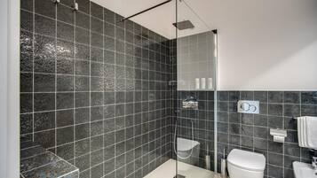 Ein modernes Badezimmer mit dunklen gemusterten Fliesen, einer gläsernen Duschkabine, einer weißen Toilette und einem Waschbecken mit Handtuchhalter.