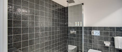 A modern bathroom with dark patterned tiles, a glass-enclosed shower, a white toilet, and a sink with a towel rack.