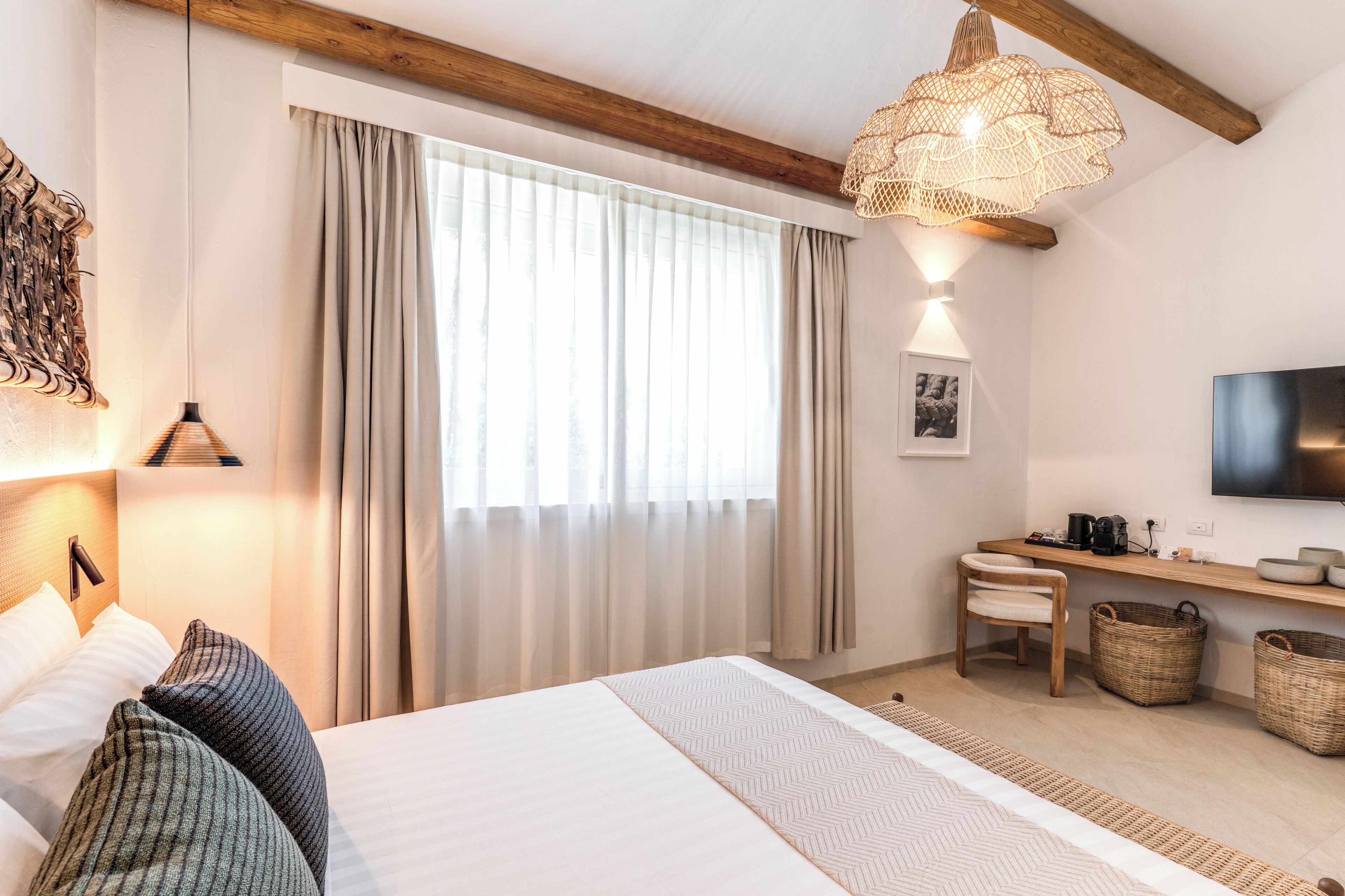 A hotel room with a bed, a desk, a chair, a television, and a large window with curtains.