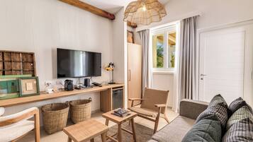 Ein möbliertes Wohnzimmer mit Fernseher, Holzmöbeln, Korbwannen und einem großen Fenster mit Vorhängen.