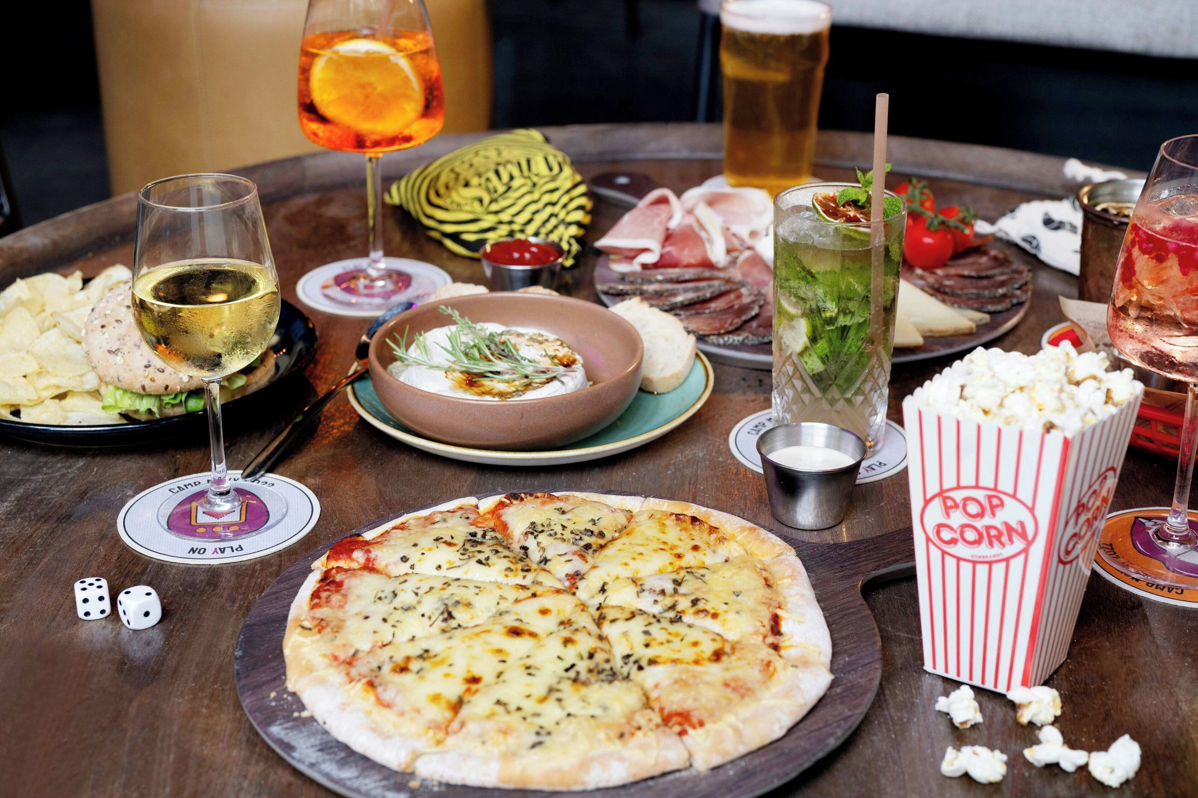 Una mesa con pizza, bebidas, aperitivos y un bol de salsa.