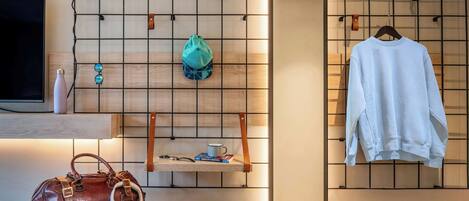 A room with a TV, a wall-mounted shelf with a bag, headphones, and books, and a hanging light fixture.