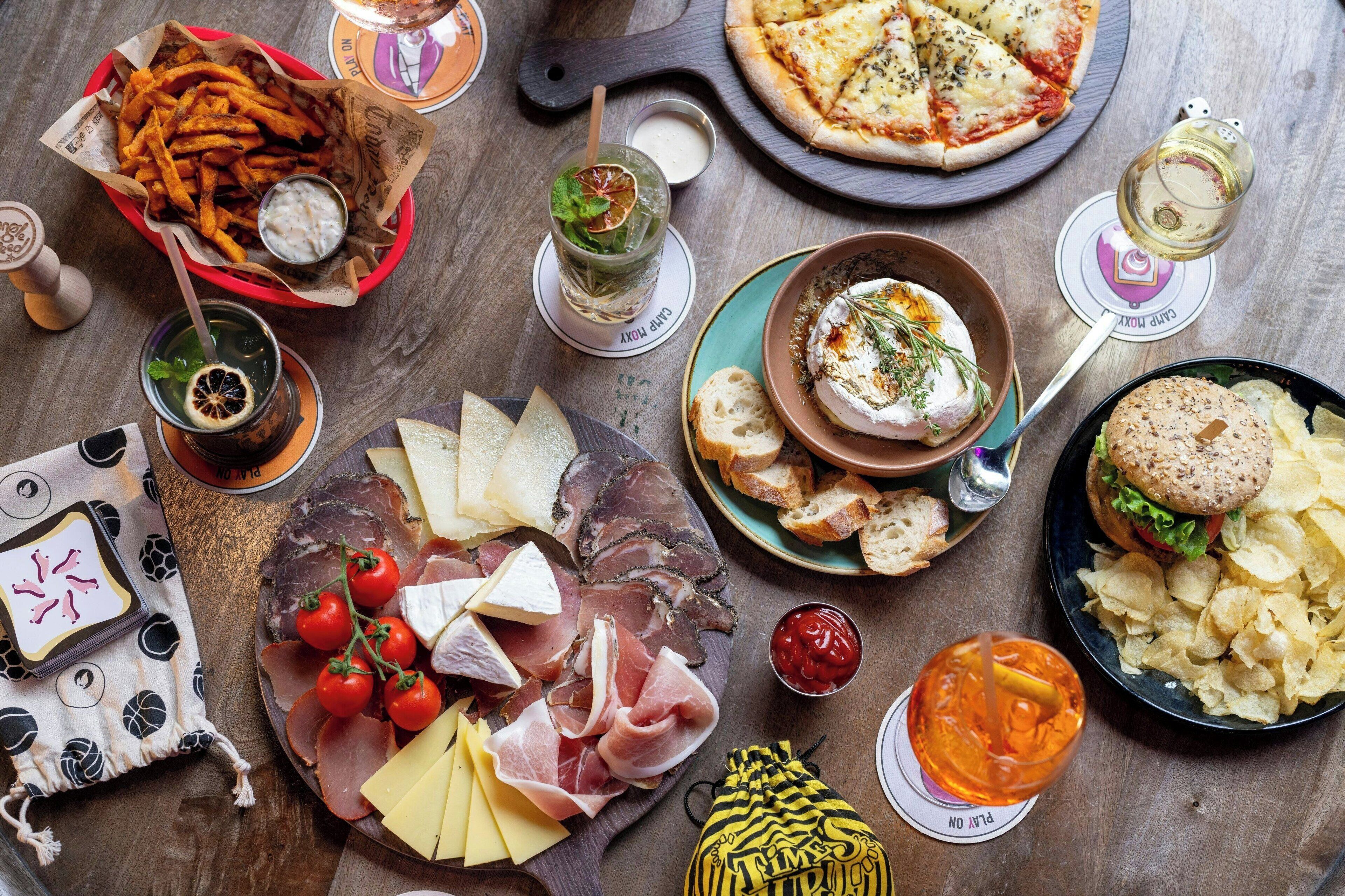 A variety of food items including cheese, meats, and a pizza on a wooden table.