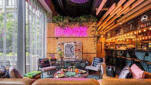 Een gezellig bargedeelte met een neonbord waarop 'DOCK' staat, houten wanden en een bar met verlichting.