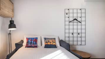 Une chambre d’hôtel bien aménagée, avec un lit, des oreillers, un luminaire suspendu, une petite table et un panneau mural avec un porte-manteau.