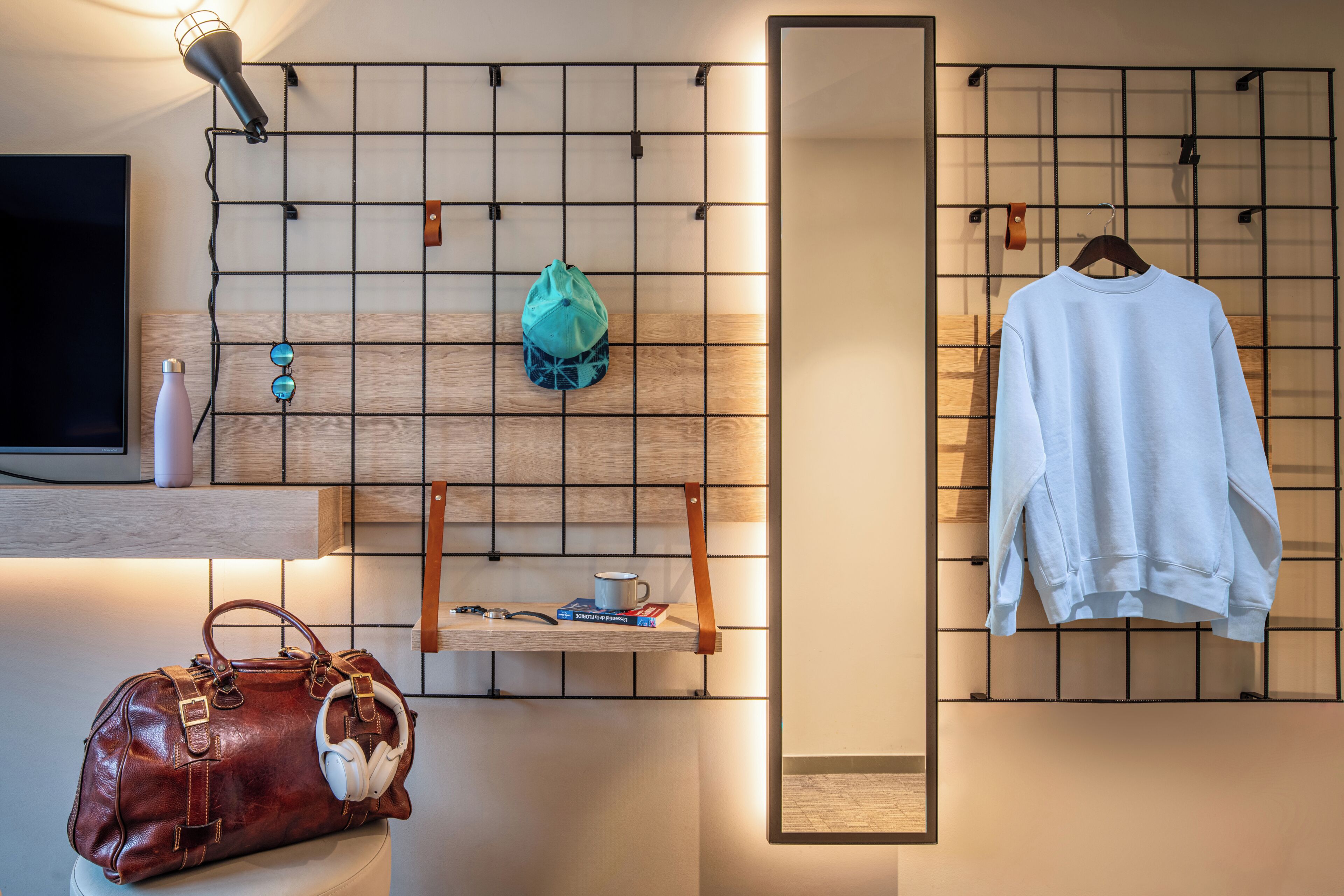 Una habitación con televisión, pared de madera, bolso colgado, sudadera blanca y repisa con libros y taza.