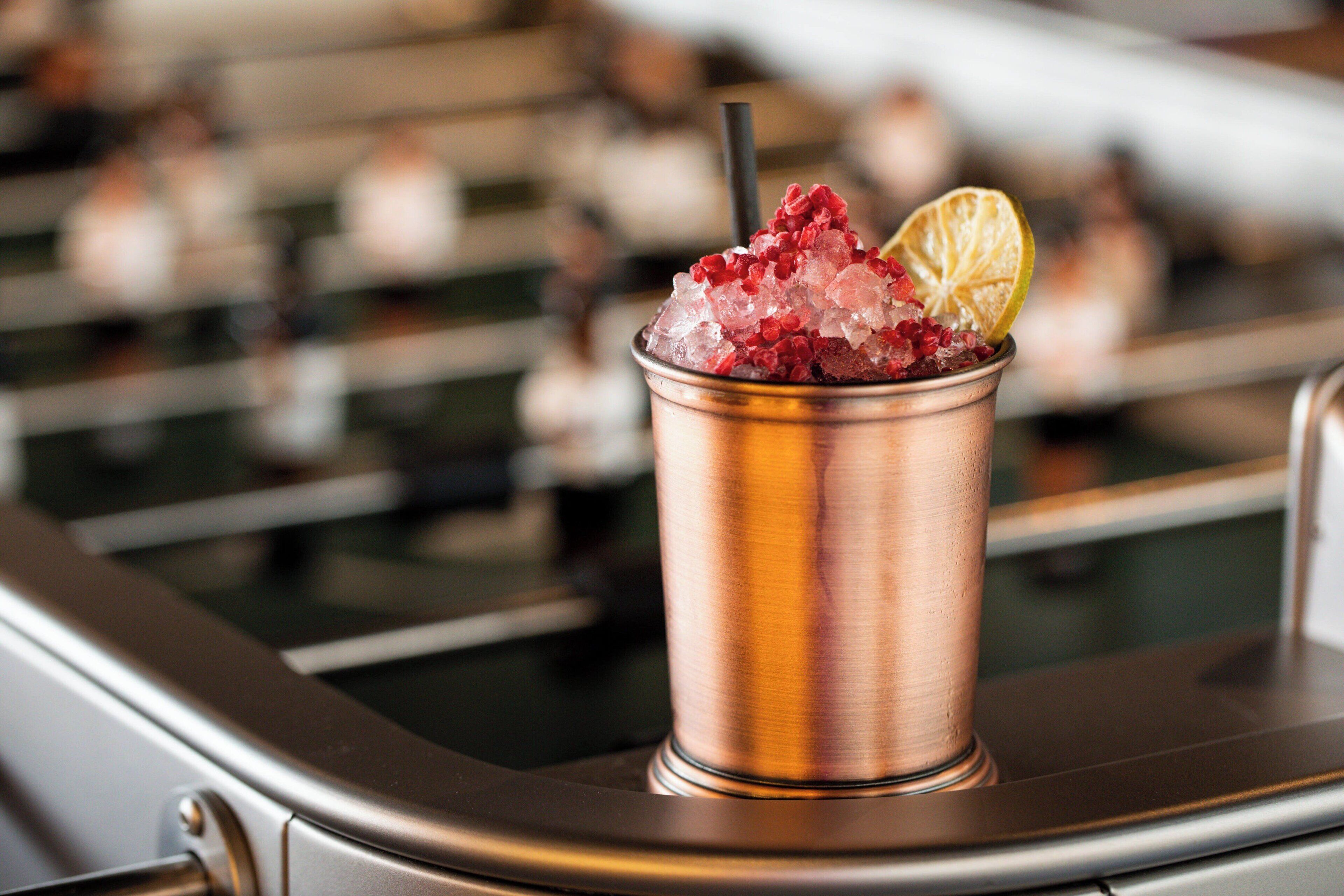 A copper drink cup with ice and a lemon slice on a bar counter.