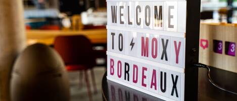 Une enseigne portant l’inscription « BIENVENUE AU MOXY BORDEAUX », dans un décor intérieur moderne.