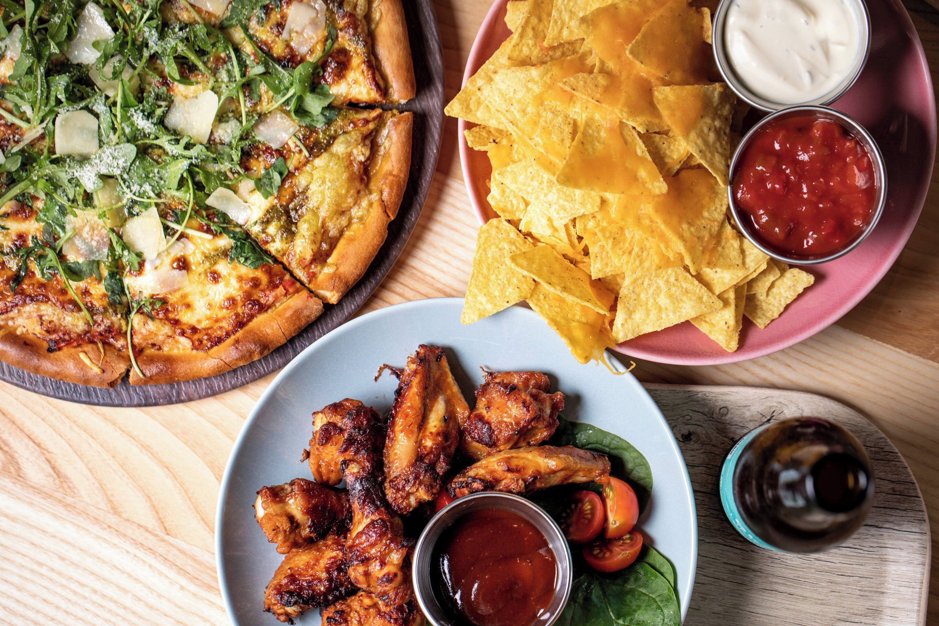 Pizza met verschillende toppings, een bord tortilla chips en twee dipsauzen.