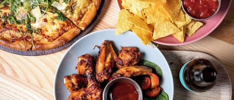Pizza met verschillende toppings, een bord tortilla chips en twee dipsauzen.