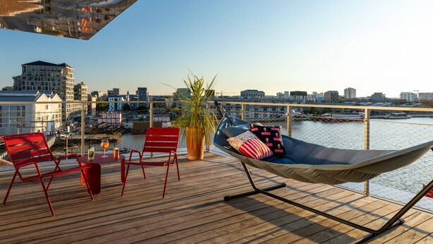 Een terras met rode stoelen, een hangmat en een plant in pot.
