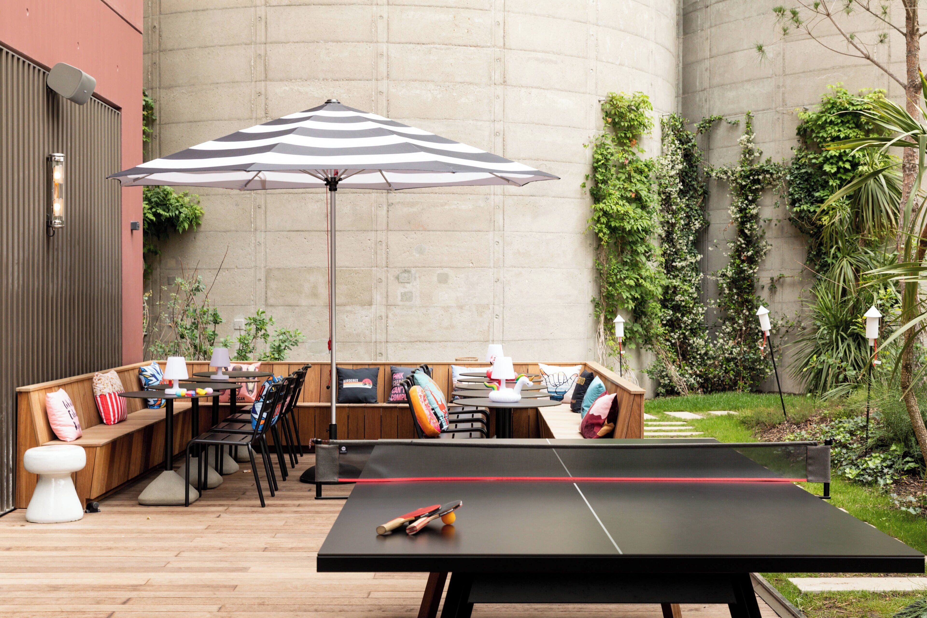 Un área de estar al aire libre con mesa de ping pong, bancos y una sombrilla.