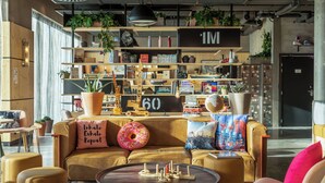 Een gezellige zithoek met een bank, salontafel en boekenkasten vol boeken en planten.