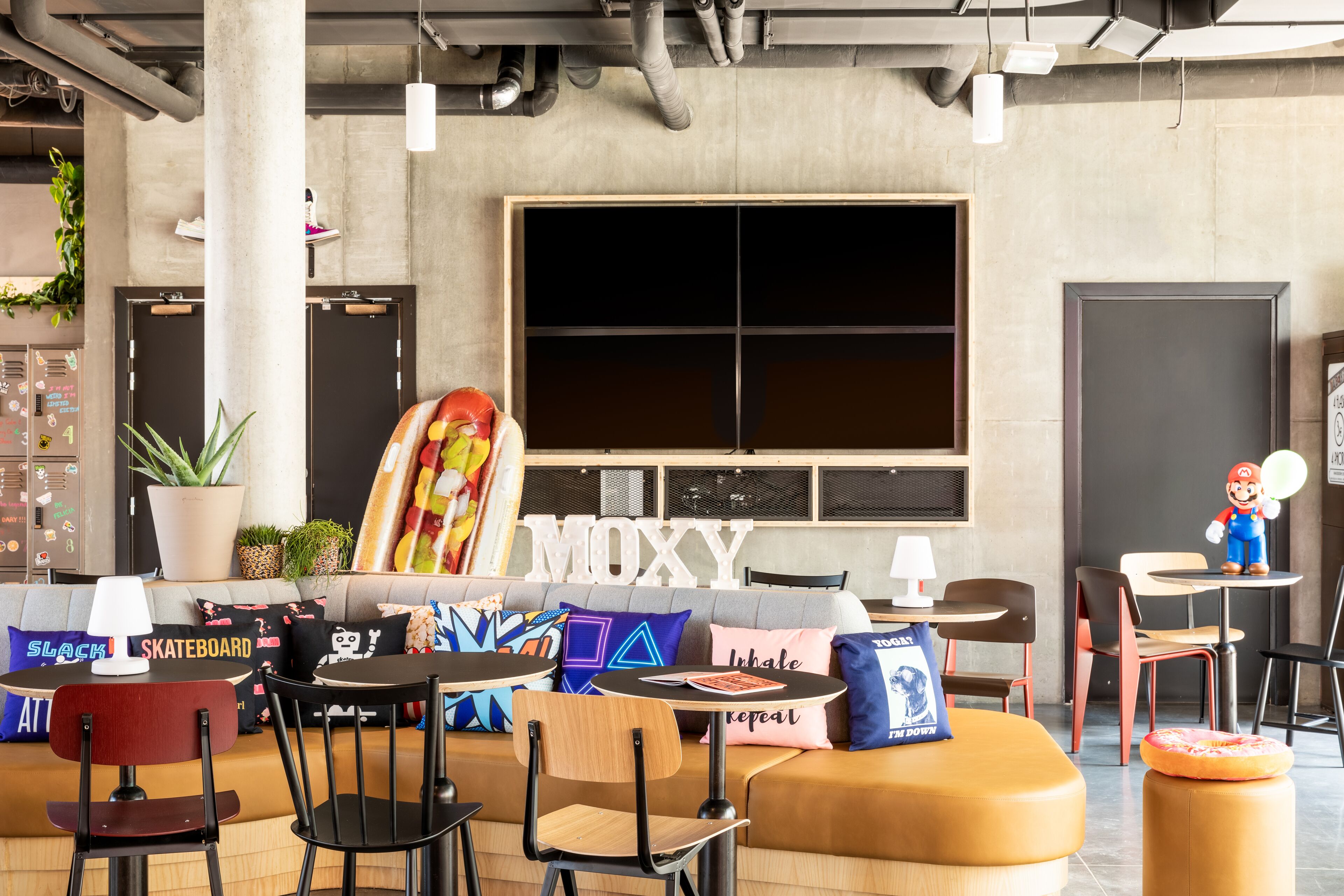 A modern lounge area with a large window, seating arrangements, and a prominent 'MOXY' sign.