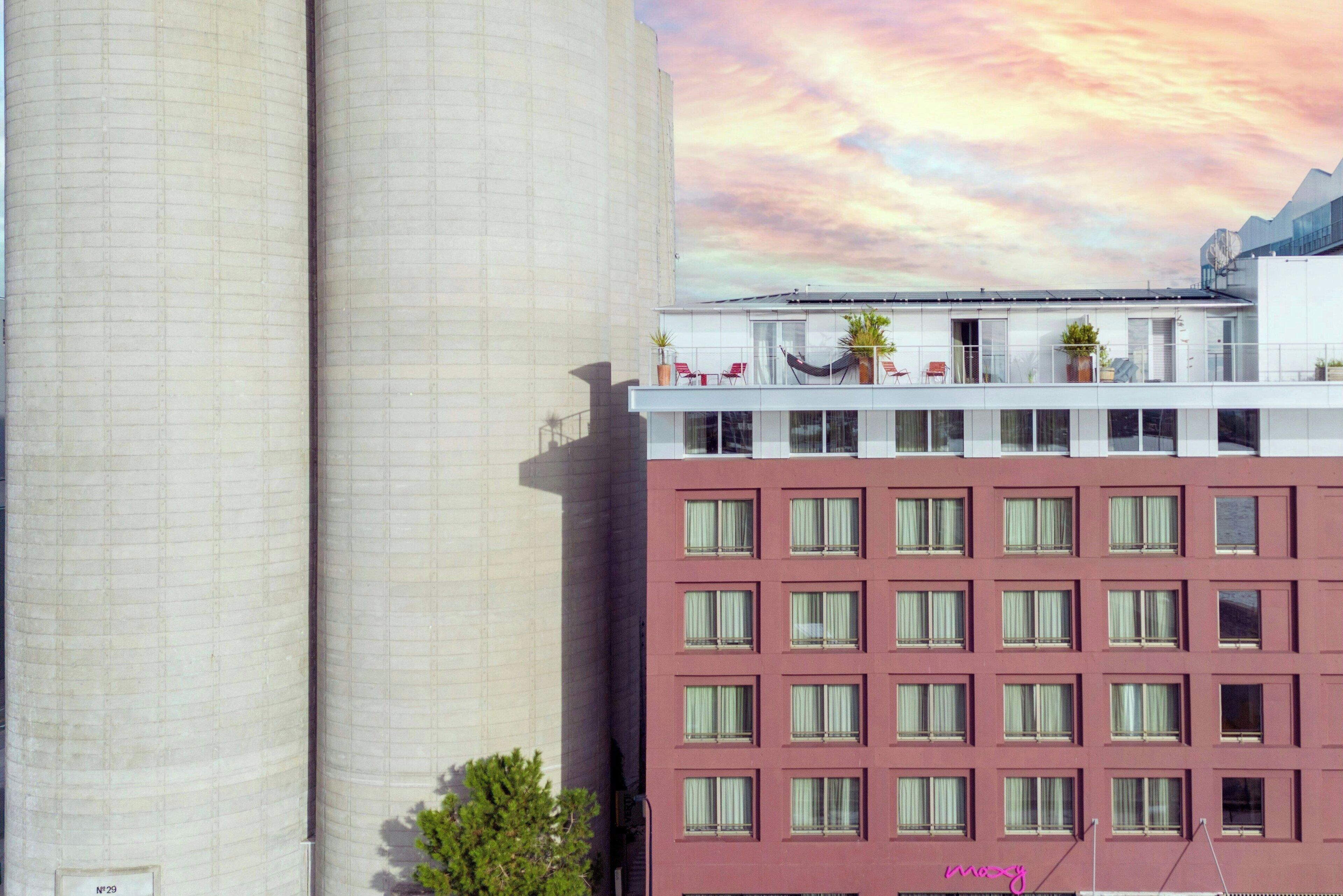 Un edificio de varios pisos con un balcón en el nivel superior, adornado con plantas en macetas y mobiliario.