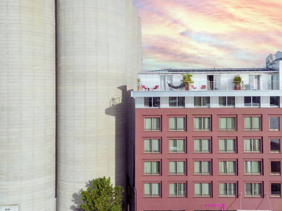 Un edificio de varios pisos con un balcón en el nivel superior, adornado con plantas en macetas y mobiliario.