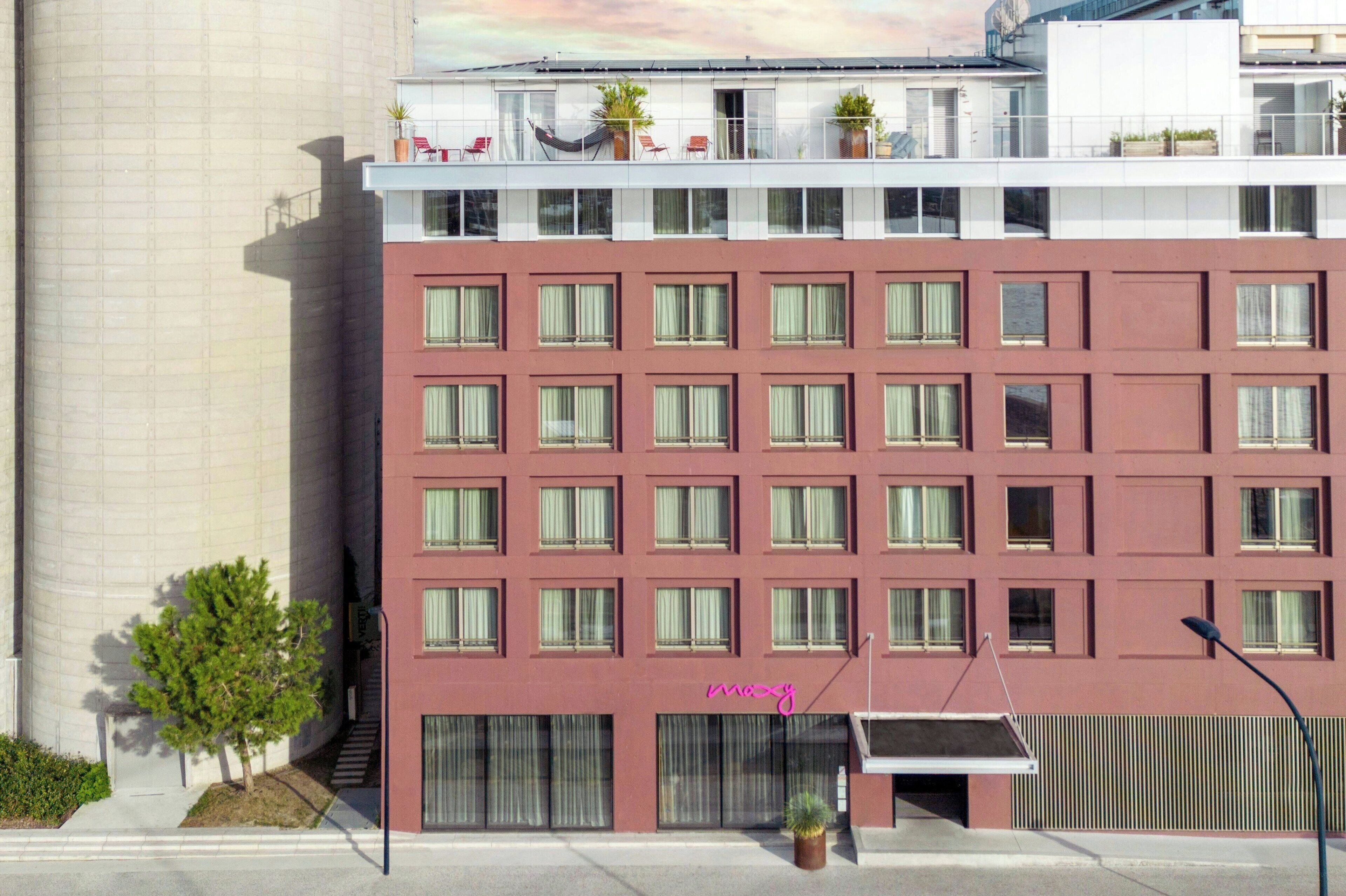 Un hotel de varios pisos con fachada roja, numerosas ventanas y un balcón con mobiliario exterior.