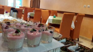 A dining area with tables set for a meal, featuring a dessert buffet with various fruit and nut toppings. - Garni Hotel Koral (Budva)