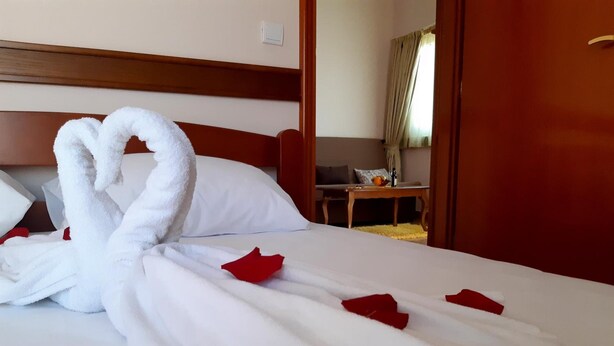 A hotel room with a bed, a wooden headboard, a nightstand with a lamp, and a window with curtains. - Garni Hotel Koral (Budva)