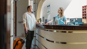 A hotel reception area with a curved counter, a reception desk, and a visible staircase. - Garni Hotel Koral (Budva)