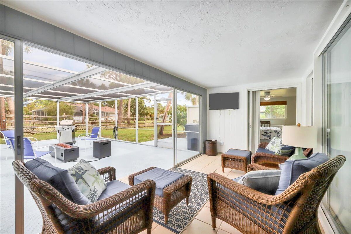 A covered patio area with wicker furniture, a grill, and a TV mounted on the wall.