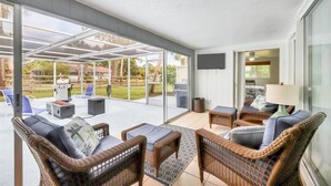 Un patio couvert aménagé avec des meubles en osier, un barbecue et un téléviseur fixé au mur.