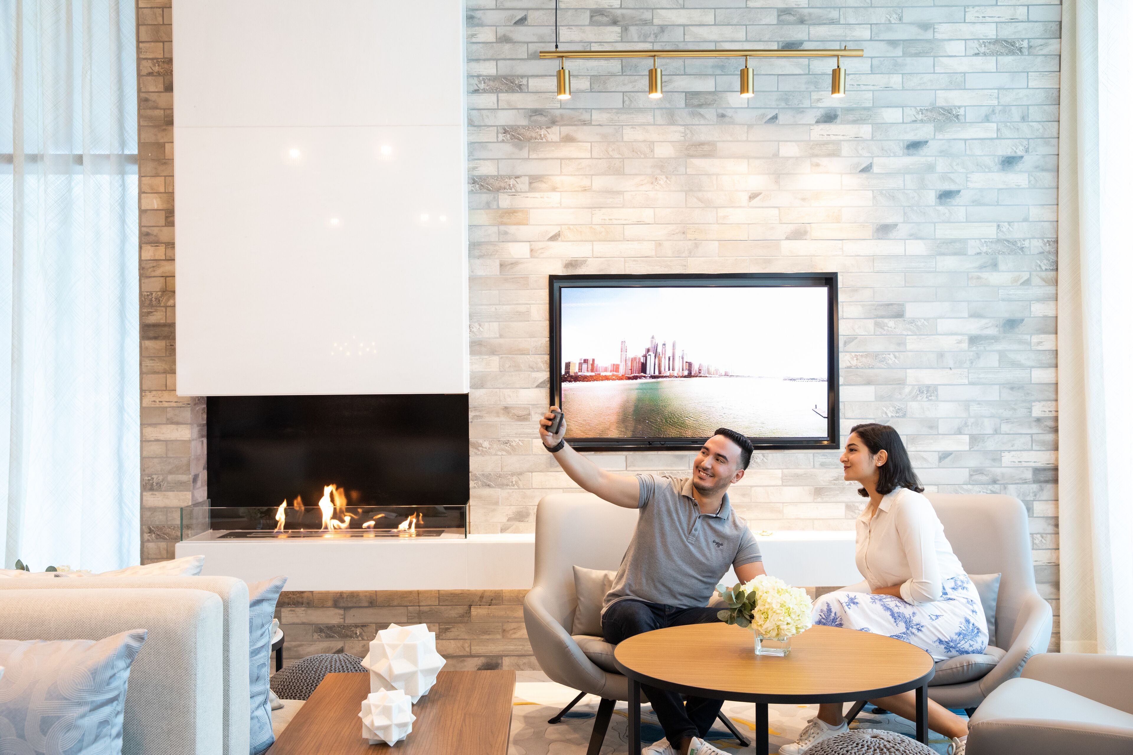 A modern living room with a fireplace, a flat-screen TV mounted on the wall, and a round coffee table with a vase of flowers.