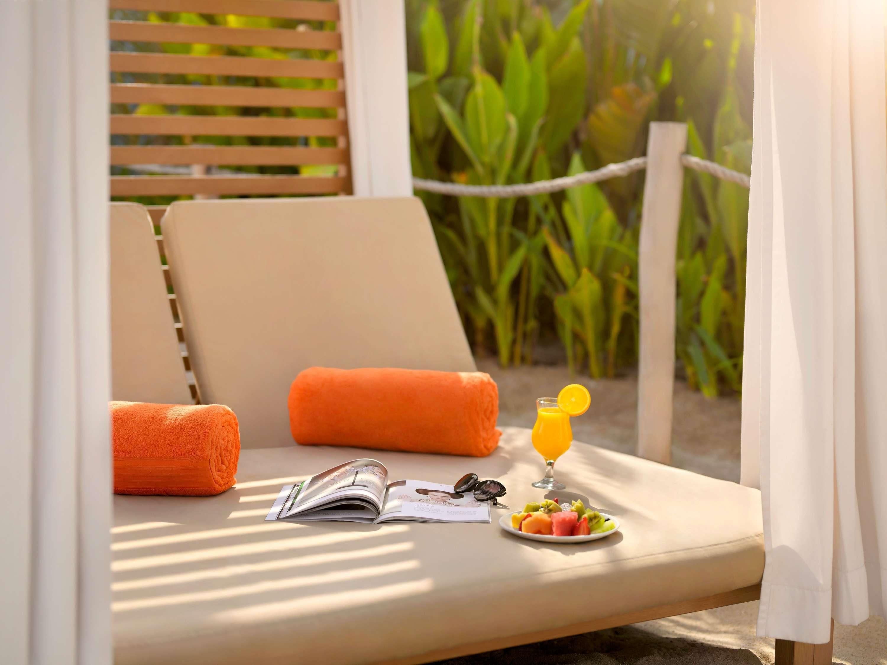 Ein sonnendurchfluteter Loungebereich mit Tisch, Zeitschrift, Sonnenbrille, Obstteller und einem Glas Orangensaft.