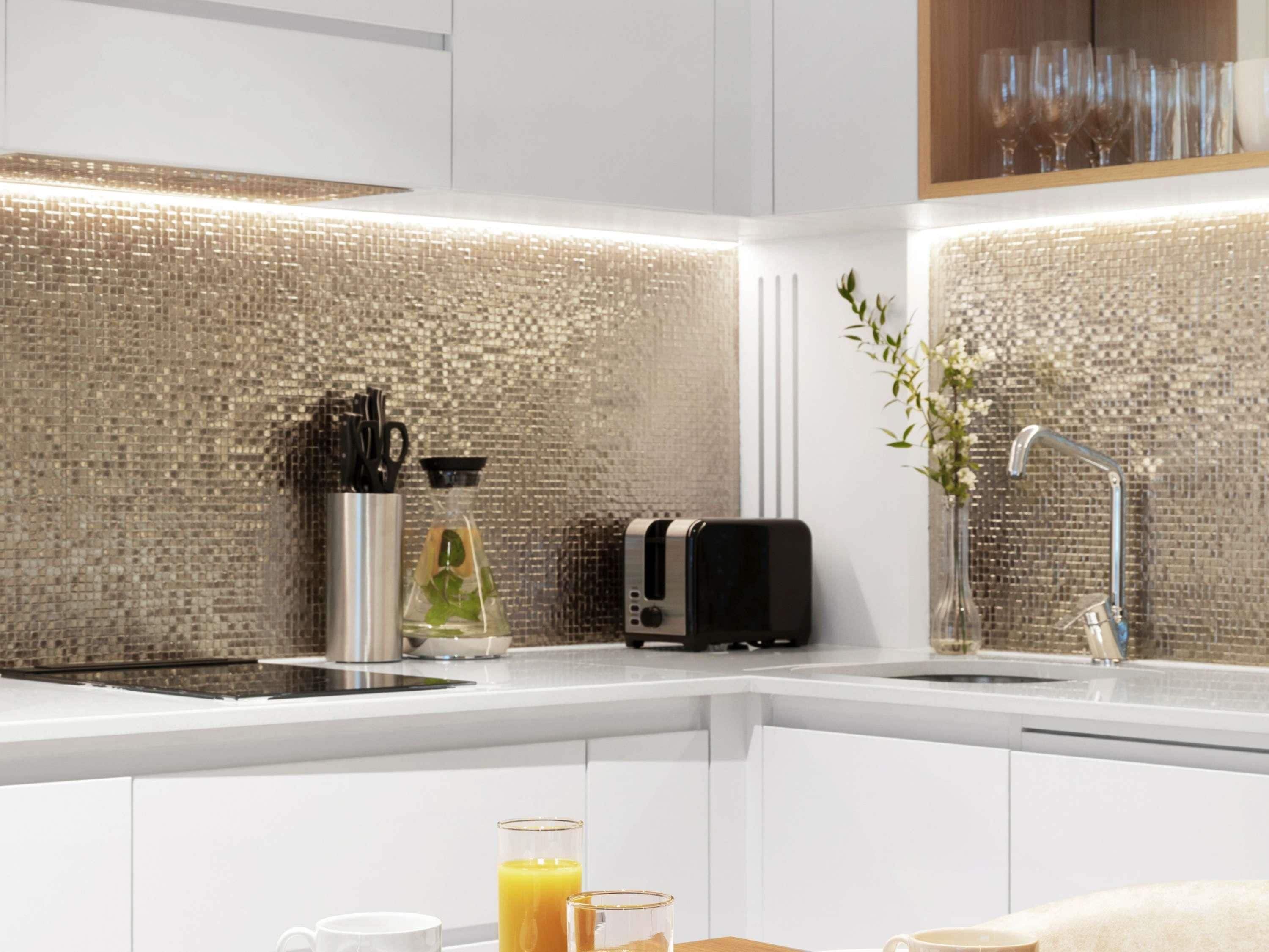 Une cuisine moderne avec un mur recouvert de mosaïques, un grille-pain, une bouilloire et un verre de jus d’orange posé sur le plan de travail.