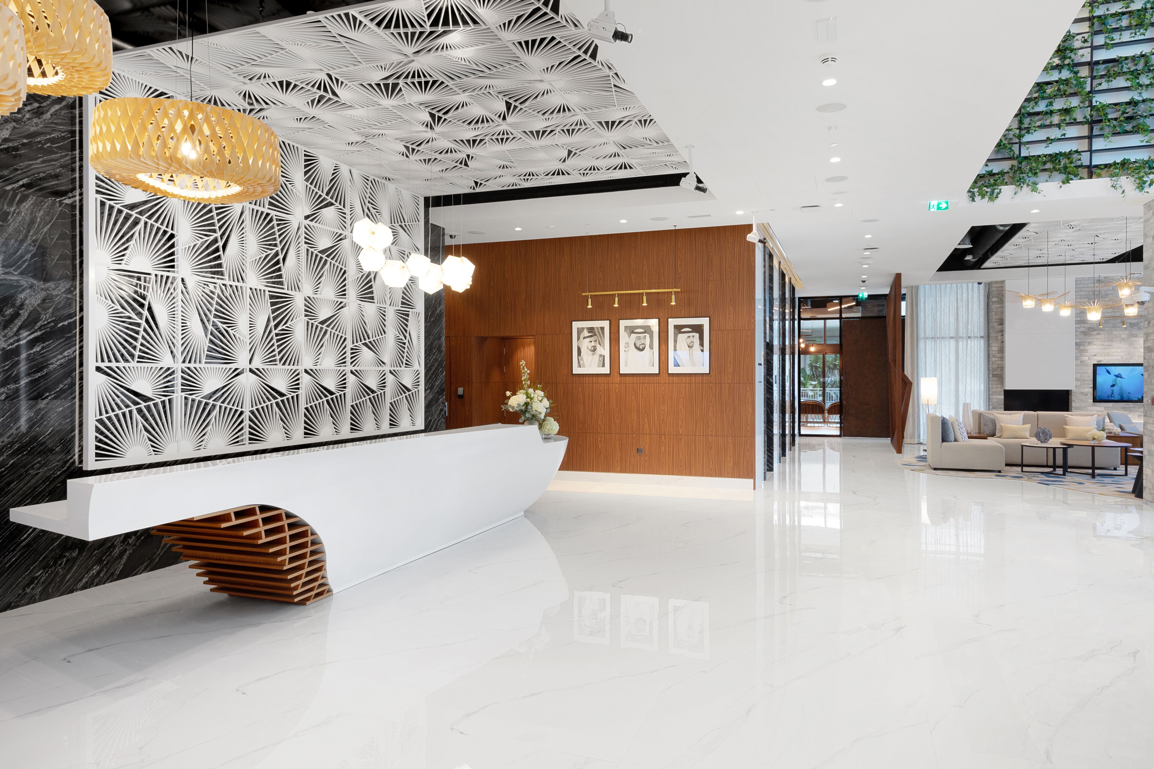 Un área de recepción moderna con un mostrador blanco, pared con diseño y un espacio de descanso con televisor.