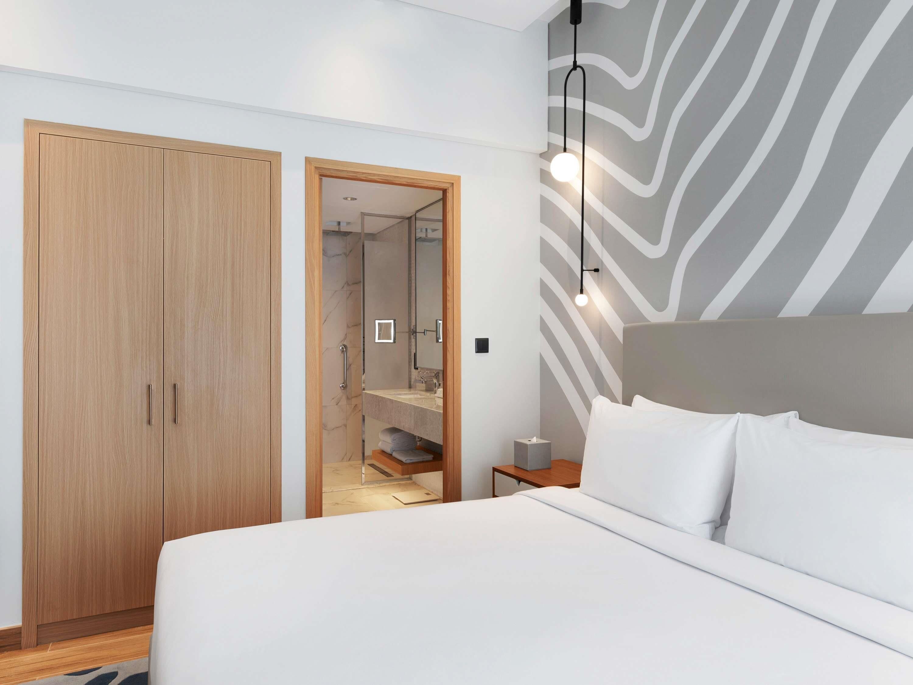 Een slaapkamer met een bed, een houten kledingkast, een nachtkastje en een muur met een golvend patroon.