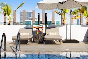 A poolside area with lounge chairs, a table, and an umbrella. - Adagio Premium The Palm (Dubai)
