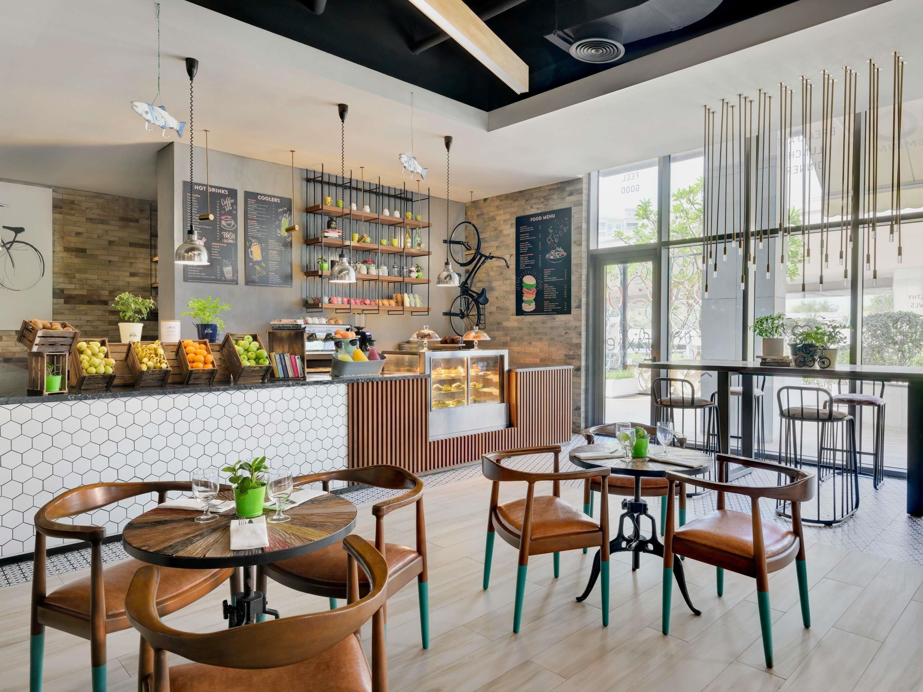 A modern cafe with wooden furniture, a variety of drinks and food displayed, and large windows offering a view of the outdoors.
