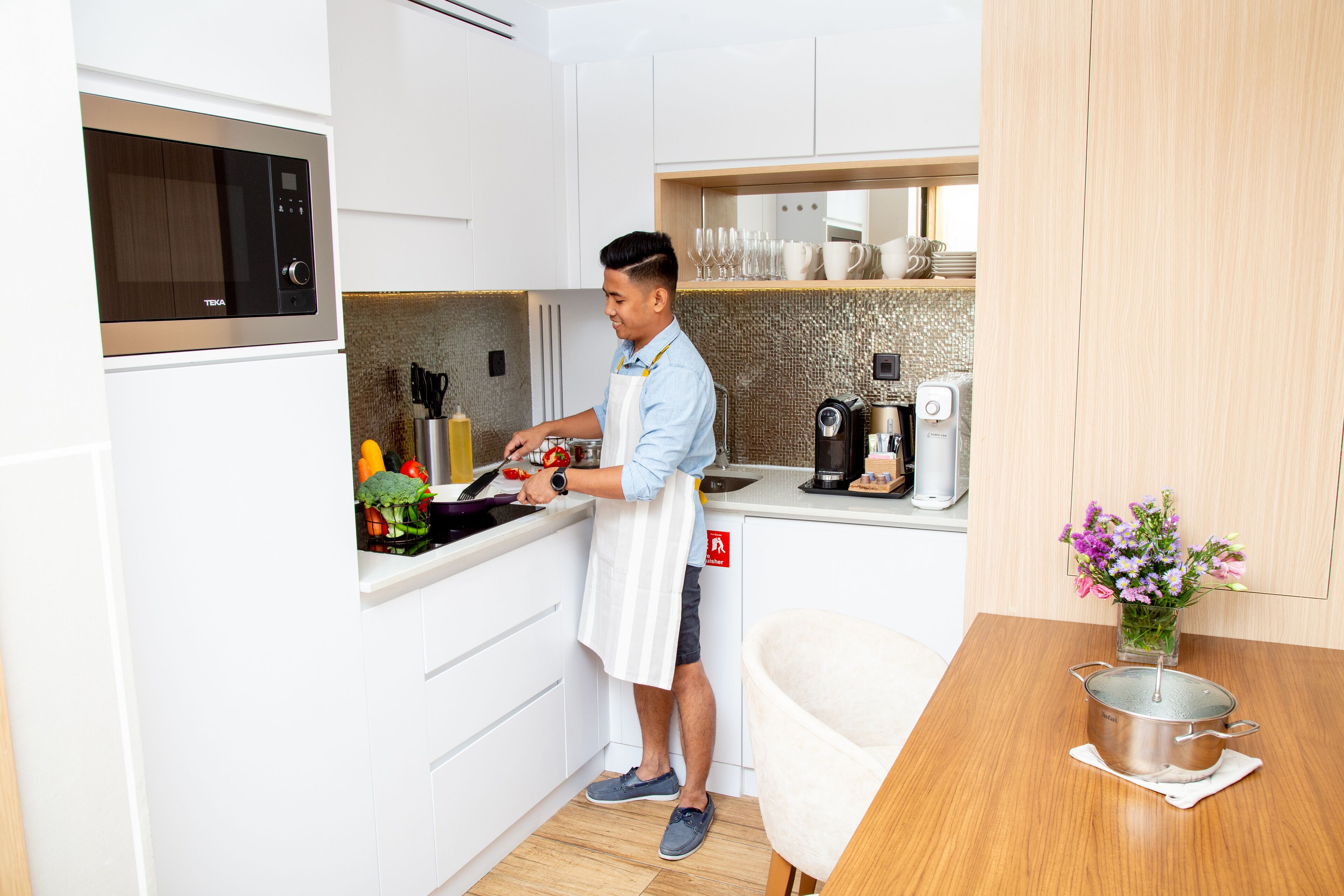 Eine moderne Küche mit weißen Schränken, einer Mikrowelle, einer Kaffeemaschine und einer Person beim Kochen.