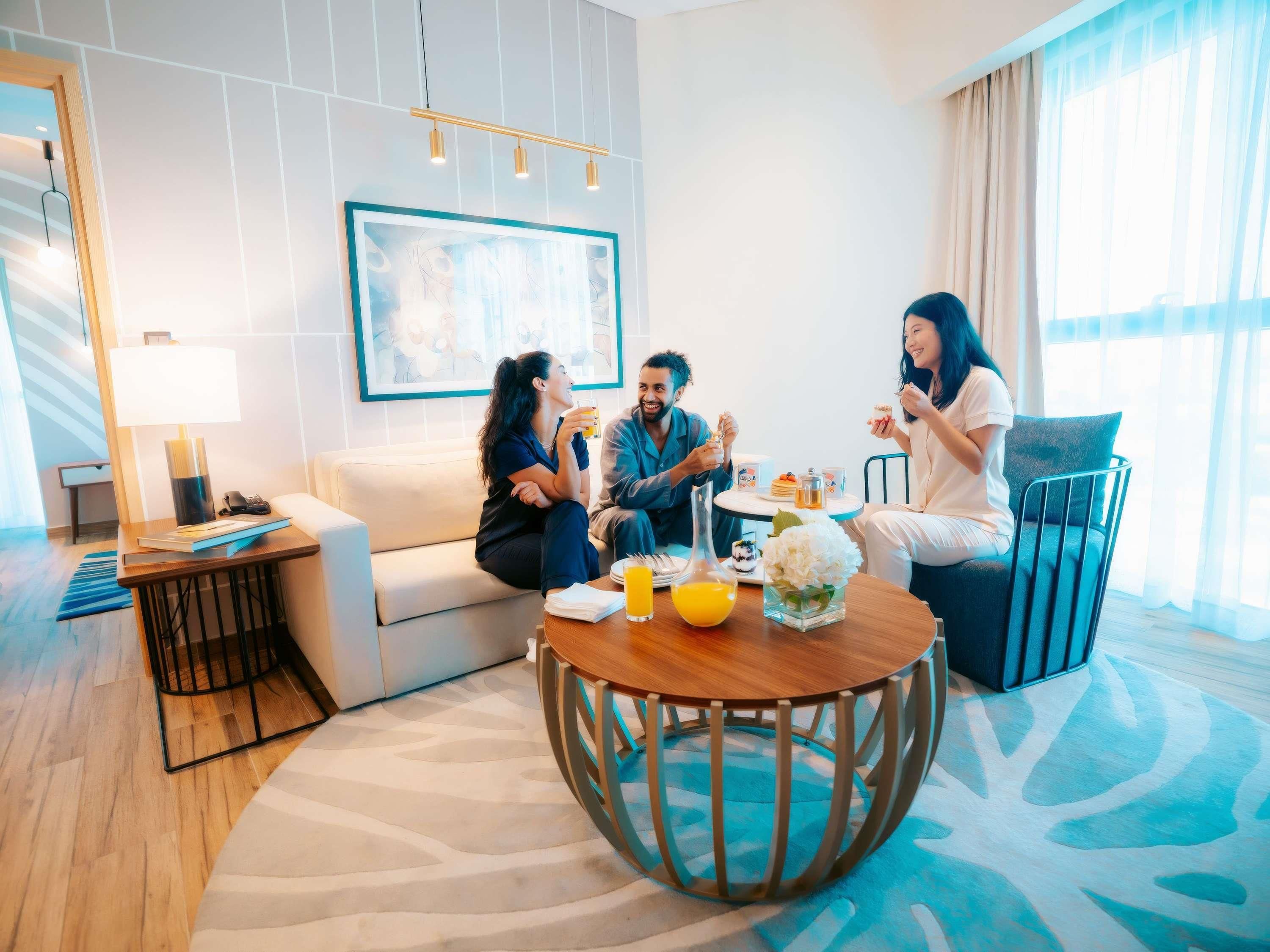 A modern hotel room with a round coffee table, a sofa, a small side table, and a painting on the wall.