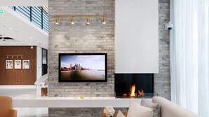 Una sala de estar moderna con chimenea, un televisor de pantalla plana montado en una pared de ladrillo y un sofá con cojines.