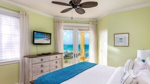 Een slaapkamer met een bed, een dressoir, een televisie en een balkon met uitzicht op de oceaan.