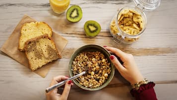A breakfast setting with bread, granola, a glass of orange juice, and a kiwi on a wooden table.