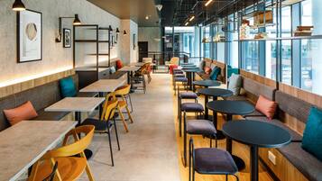 Un café moderne doté de longues tables communes, de sièges individuels et de grandes fenêtres offrant une vue dégagée.