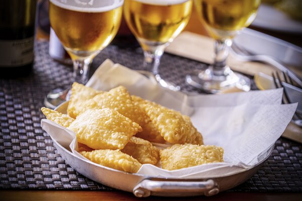 Una cesta de aperitivos fritos sobre una mesa, con una botella y vasos de cerveza al fondo.