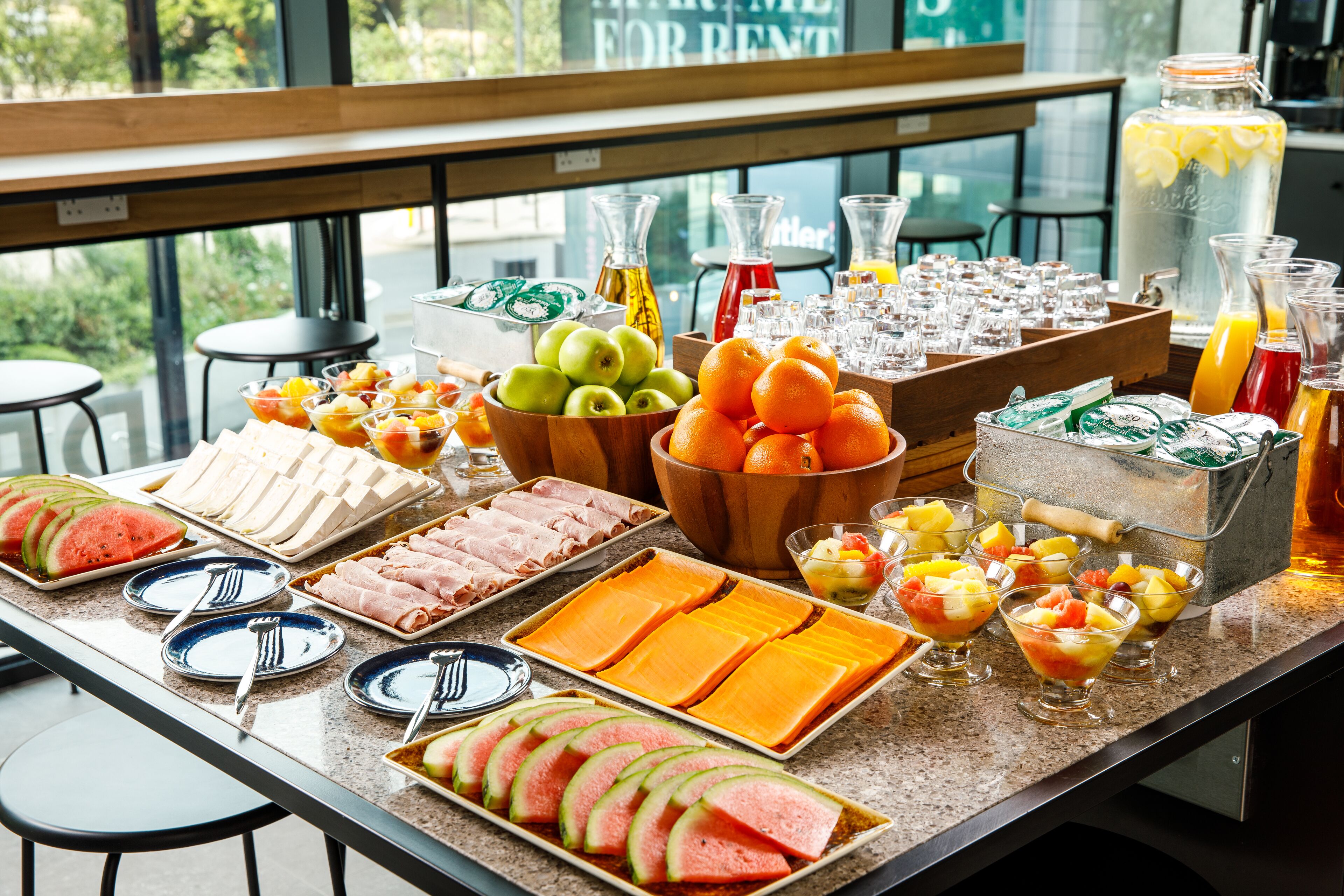 A breakfast buffet with various fruits, cheeses, and beverages.