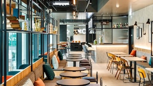 Una cafetería moderna con mesas y bancos redondos, un área de bar y estanterías con diversos objetos.