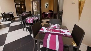Comedor con mesas dispuestas para dos, con piso a cuadros blanco y negro y manteles a rayas rosas y blancas.