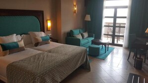 Habitación de hotel con dos camas, un sofá, un escritorio y un balcón con vistas.