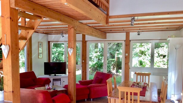 Amplia sala de estar con techo de madera, sofás rojos, una mesa de comedor de madera y un televisor.