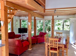 Een ruime woonkamer met een houten plafond, rode banken, een houten eettafel en een televisie.