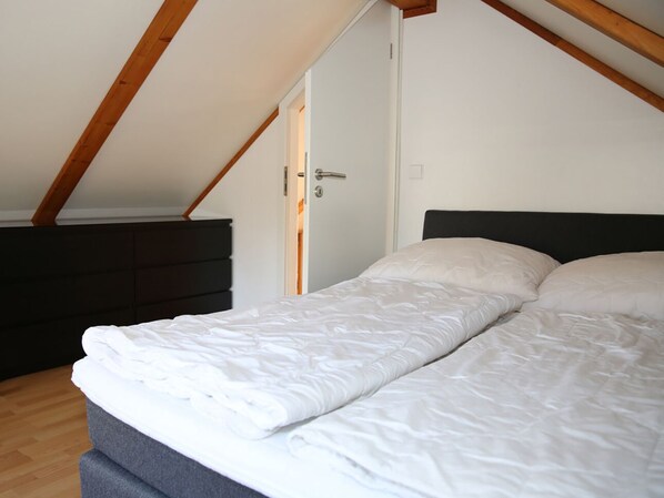 Een slaapkamer met een bed, houten balken, een deur en een donker hoofdeinde.