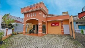 Un hotel llamado "HOTEL MUTIARA" con fachada roja y naranja, un acceso pavimentado y una motocicleta estacionada afuera.