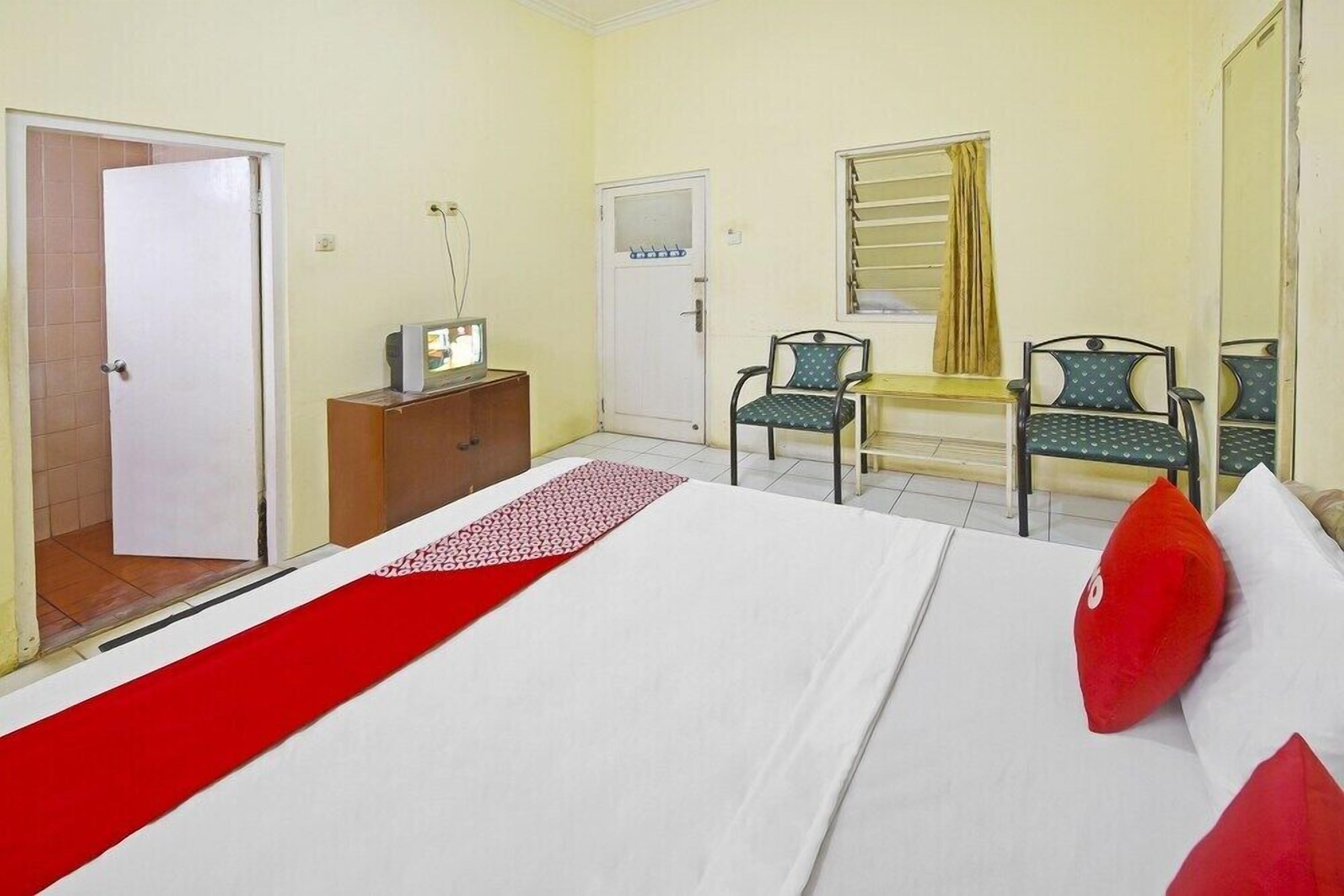 A hotel room with a bed, a desk with a computer, two chairs, a wardrobe, and a mirror.