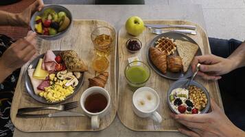 Un plat de petit esmorzar amb diferents aliments i begudes, com torrades, ous, fruita i un croissant.